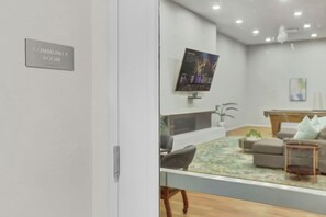 A modern community room with a glass partition, a mounted TV, and a pool table. - PremiumStays: Modern : Central to sports, arena, Theater : Loft : Parking : Gym (Cleveland)