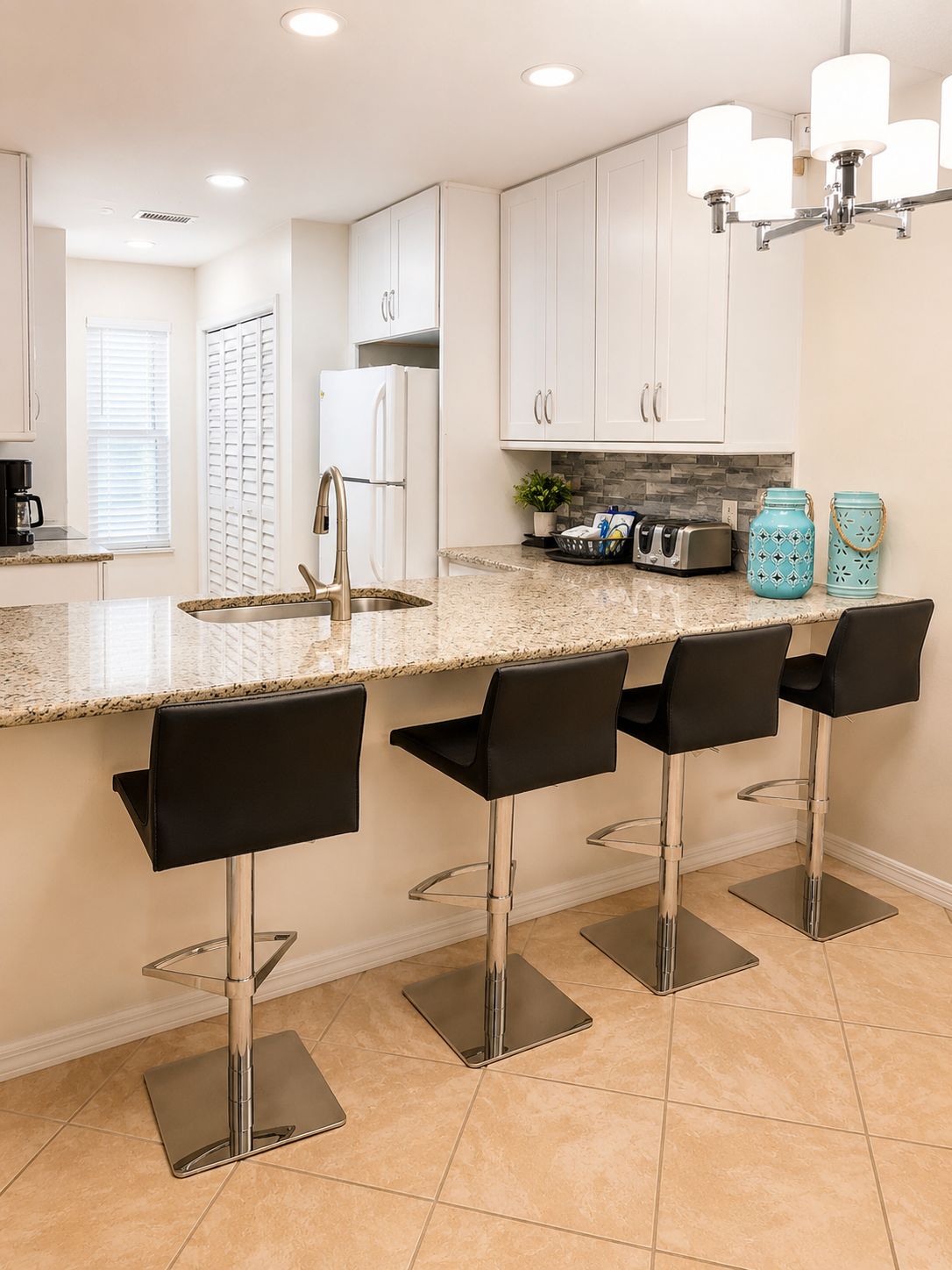 A kitchen with white cabinets, a granite countertop, a stainless steel sink, and four black bar stools.