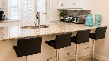 A kitchen with white cabinets, a granite countertop, a stainless steel sink, and four black bar stools.