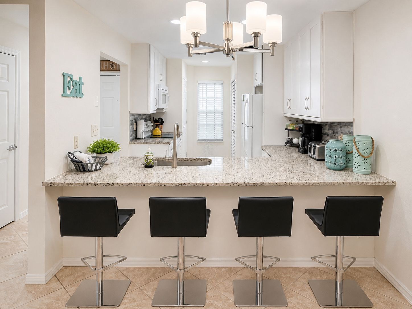 A kitchen with a marble countertop, stainless steel appliances, and three black bar stools.
