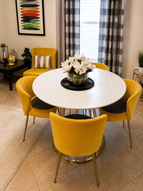 A dining area with a round table, yellow chairs, and a vase of white flowers.