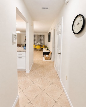 A hallway with a kitchen area, a dining table, and a clock on the wall.