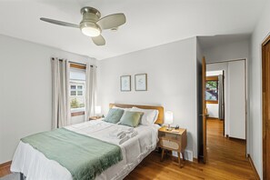 A bedroom with a bed, bedside tables, a ceiling fan, and a view of the outside.