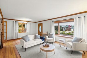 A living room with a sofa, two armchairs, a coffee table, and a view of a residential street.