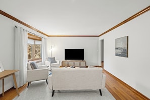 A living room with a flat-screen TV, two armchairs, a sofa, and a wooden floor.