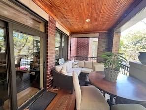 Ein überdachter Patio-Bereich mit Holzboden, einer Couch, einem Tisch und einem Blumentopf.