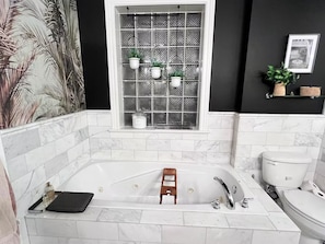 Ein Badezimmer mit einer großen Badewanne, einem Fenster mit Pflanzen, einer Toilette und einer Duschkabine.
