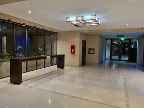 A modern hotel lobby with a checkered floor, a reception desk, a glass partition, and a ceiling light fixture. - Two-room apartment - Macrocentro Salta (Salta)