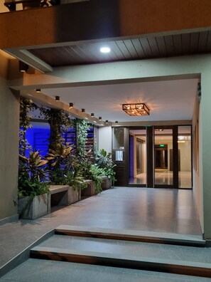 A modern hotel lobby with a central staircase, a decorative ceiling light, and a variety of indoor plants. - Two-room apartment - Macrocentro Salta (Salta)