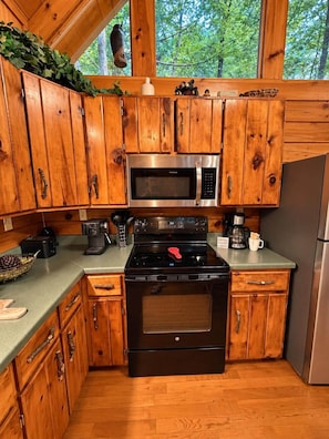 A kitchen with wooden cabinets, a stainless steel microwave, a stove, and a refrigerator. - A Piece of Paradise| Pigeon Forge Cabin| Hot Tub (Sevier County)