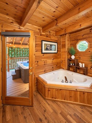 A wooden cabin interior with a large bathtub, a framed picture on the wall, and a window with a view. - A Piece of Paradise| Pigeon Forge Cabin| Hot Tub (Sevier County)