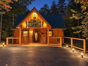 Une cabane en rondins dotée d’un porche à l’avant, d’une porte d’entrée décorative et d’un petit espace porche avec une chaise.