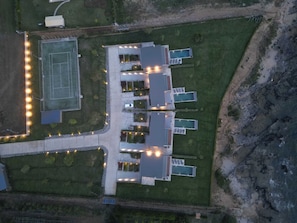An aerial view of a building with multiple swimming pools, a tennis court, and a parking area. - Real Life Homes (Pyrgos)
