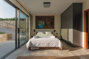 A modern bedroom with a large bed, a painting above it, and a view through a glass door. - Real Life Homes (Pyrgos)