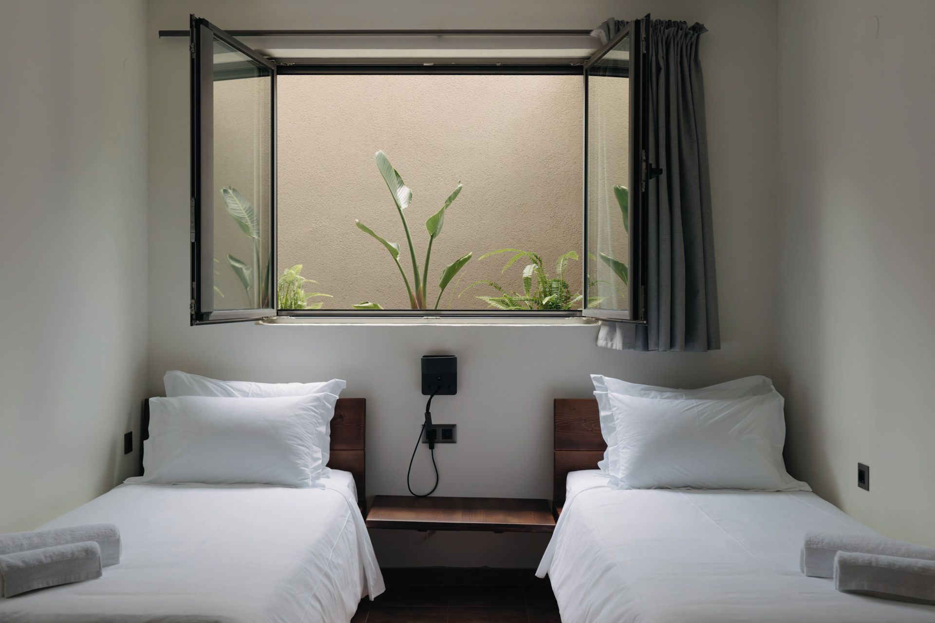 Una habitación con dos camas, una ventana con vistas a plantas y un enchufe en la pared.