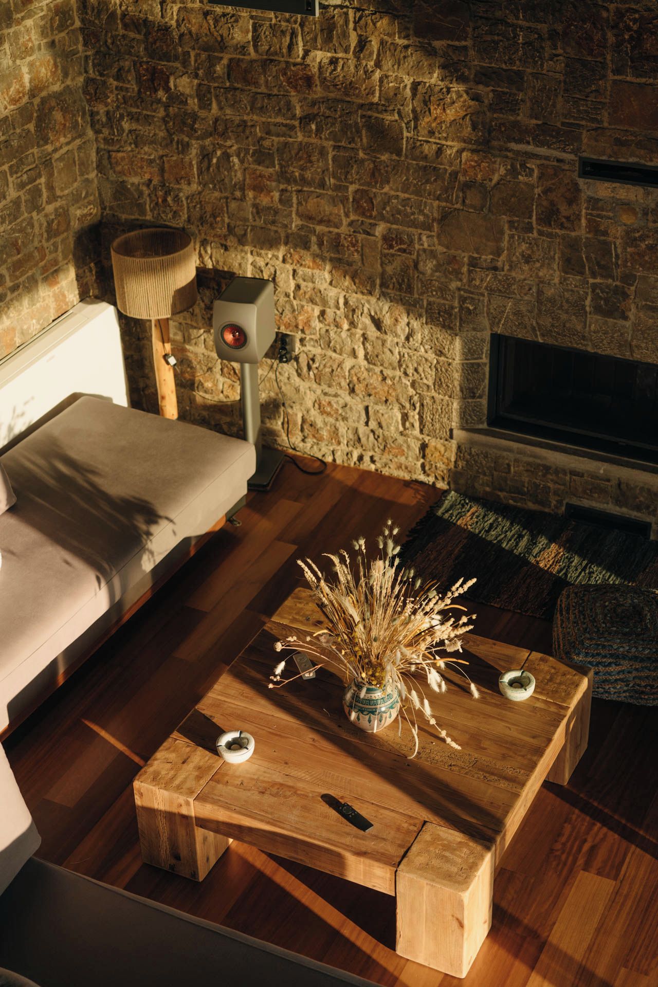 A cozy room with a stone wall, a fireplace, a sofa, and a coffee table with a vase.