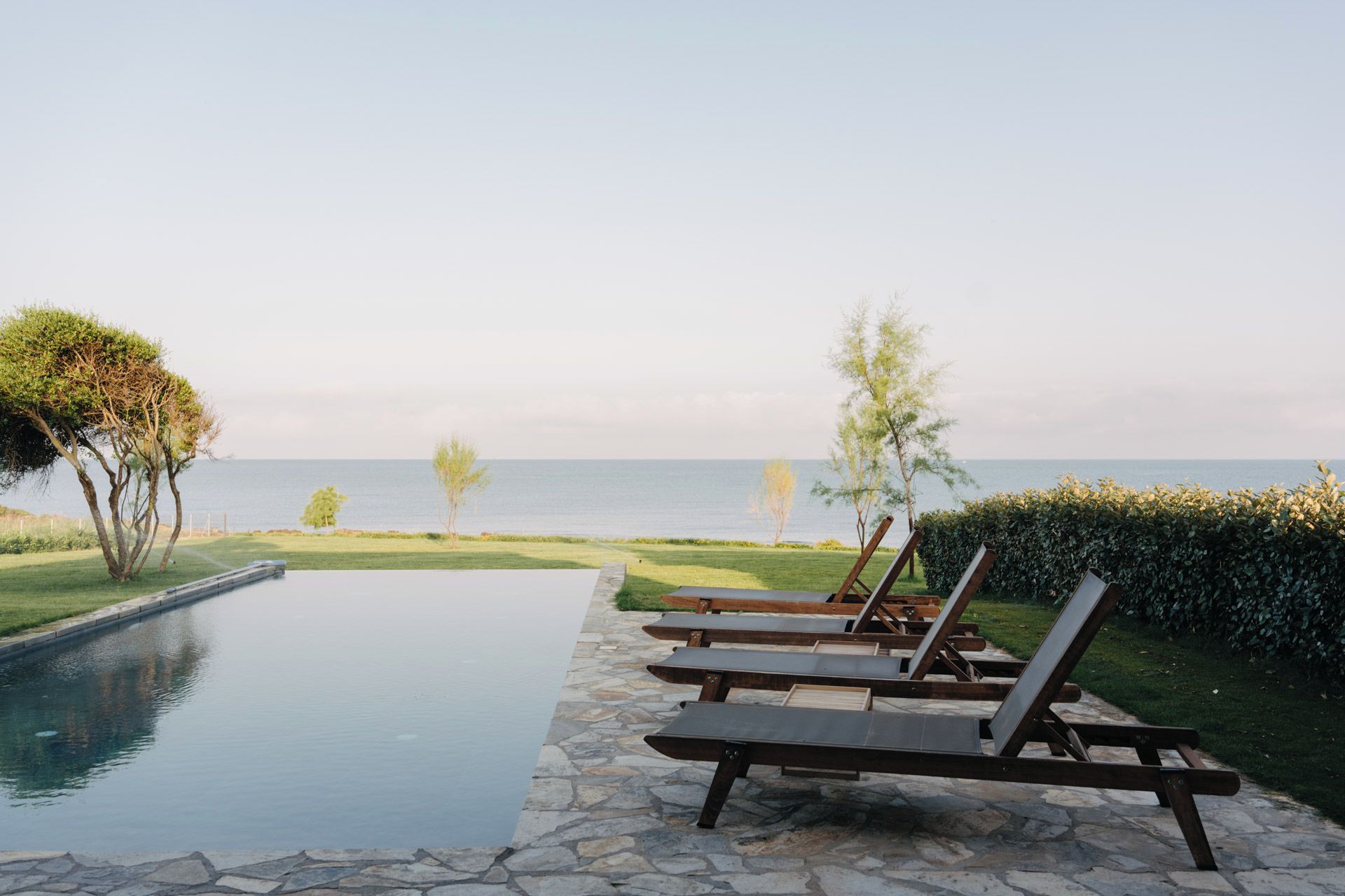 Zona de piscina con sillas de descanso y vista al mar.