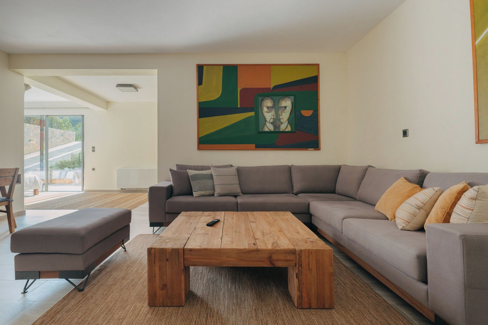 A modern living room with a sectional sofa, a wooden coffee table, and a colorful abstract painting on the wall.