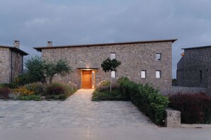 A stone building with a central entrance, surrounded by a stone pathway and various plants.