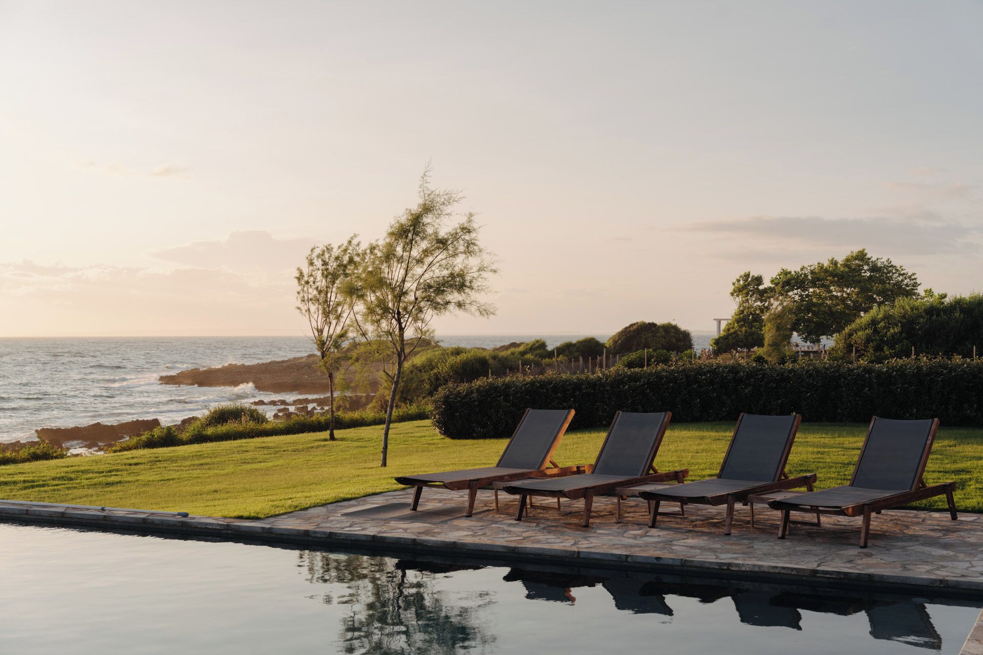 Área de piscina com espreguiçadeiras e vista para o mar.