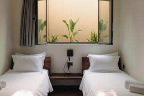 Une chambre d’hôtel avec deux lits, une fenêtre donnant sur des plantes et une prise électrique au mur.