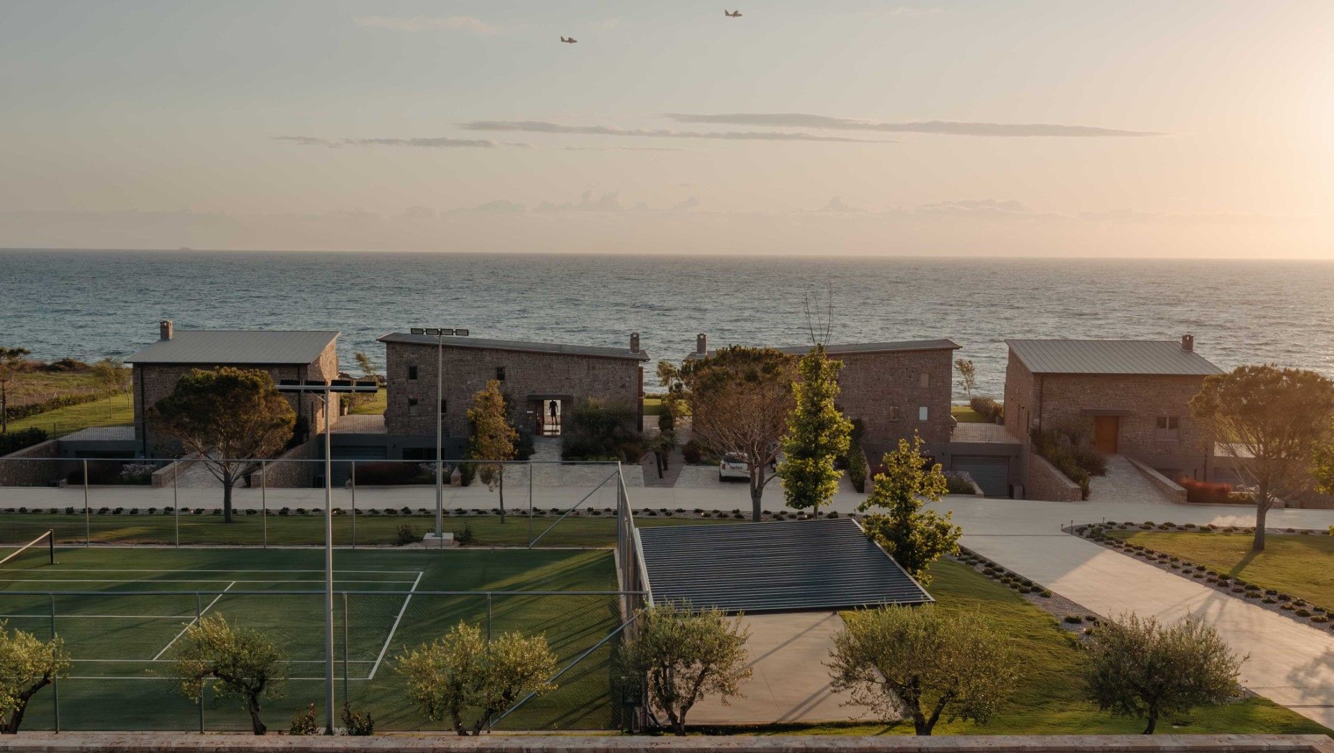 Una propietat costanera amb pista de tennis, edificis de pedra i vista al mar.