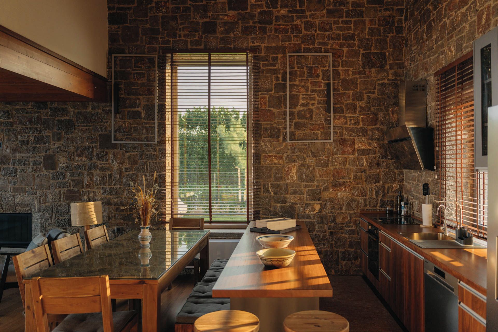 A modern kitchen with a stone wall, a large window, and a dining area with a long table and chairs.