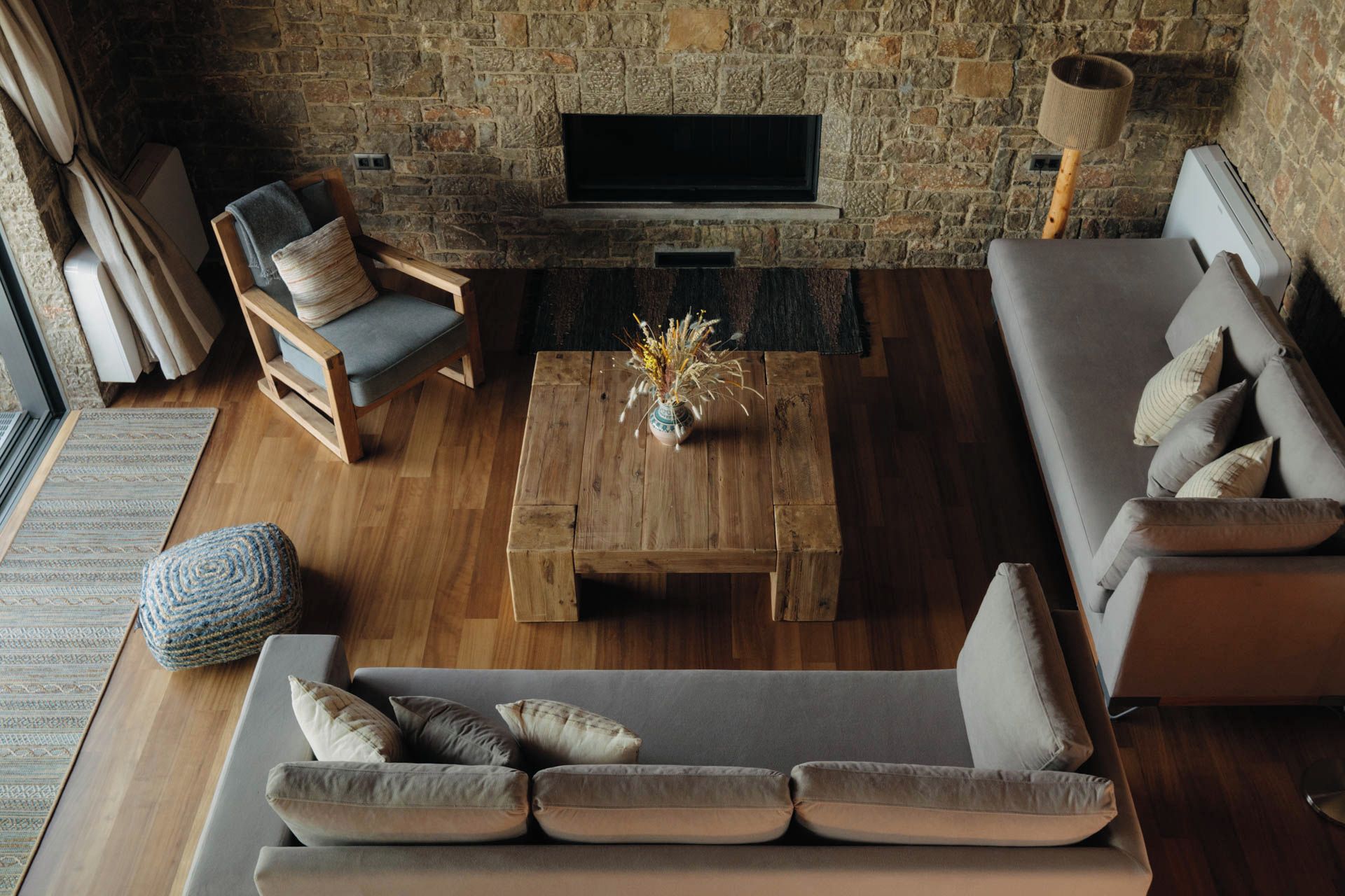 Un salon chaleureux avec une cheminée en pierre, un canapé, une table basse en bois et un fauteuil.