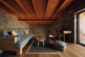Une pièce chaleureuse avec un mur en pierre, des poutres en bois, un canapé, un petit tabouret et une table en bois.
