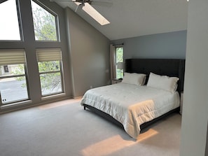 A bedroom with a bed, large windows, a ceiling fan, and a view of the outdoors.