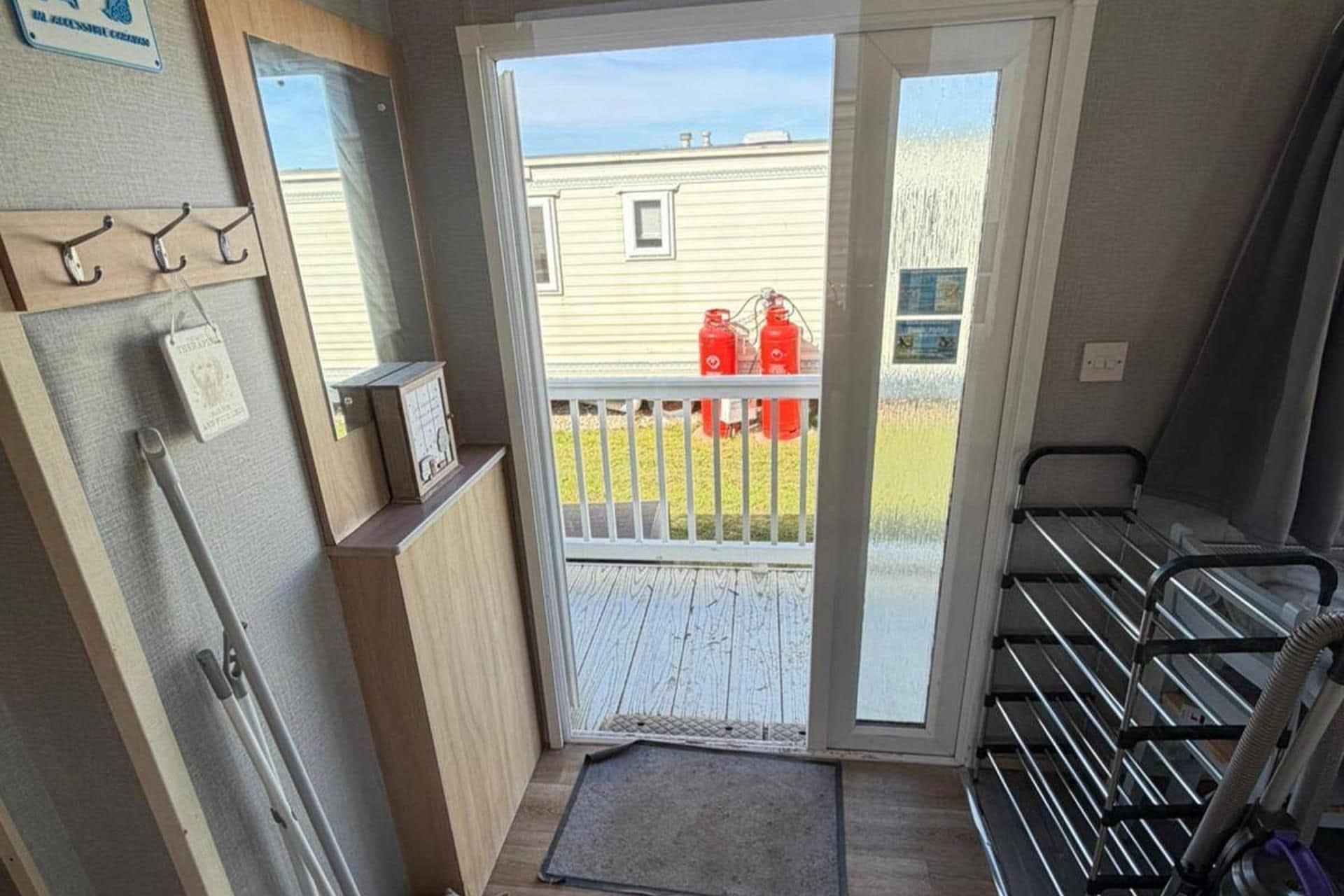 A doorway leading to a balcony with a view of a house and red fire extinguishers.
