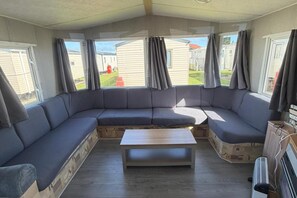 Ein Caravan-Innenraum mit einer gebogenen Couch, einem zentralen Tisch und einer Küchenzeile.