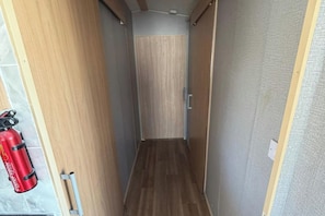 Ein schmaler Korridor mit Holzwänden und Holzboden, der zu einer Tür führt. Ein roter Feuerlöscher ist links an der Wand angebracht.