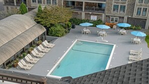 Un espace piscine aménagé sur le toit, avec des chaises longues et des parasols, entouré de verdure et bordé d’un bâtiment doté d’un toit incurvé.