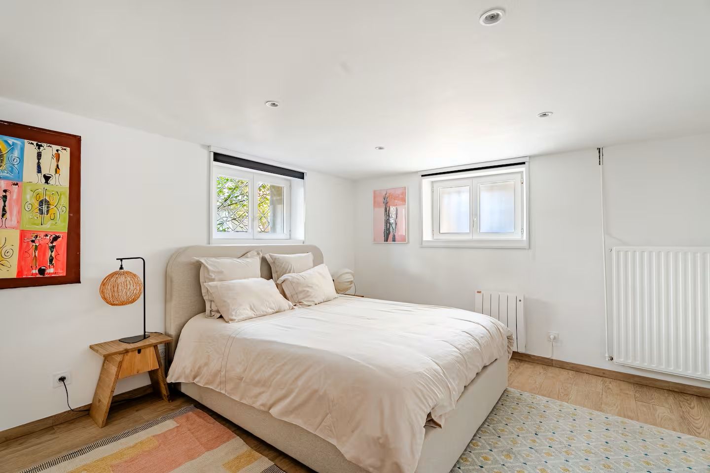 Une chambre à coucher comprenant un lit, une table de chevet, une lampe, un radiateur et des œuvres d’art accrochées aux murs.