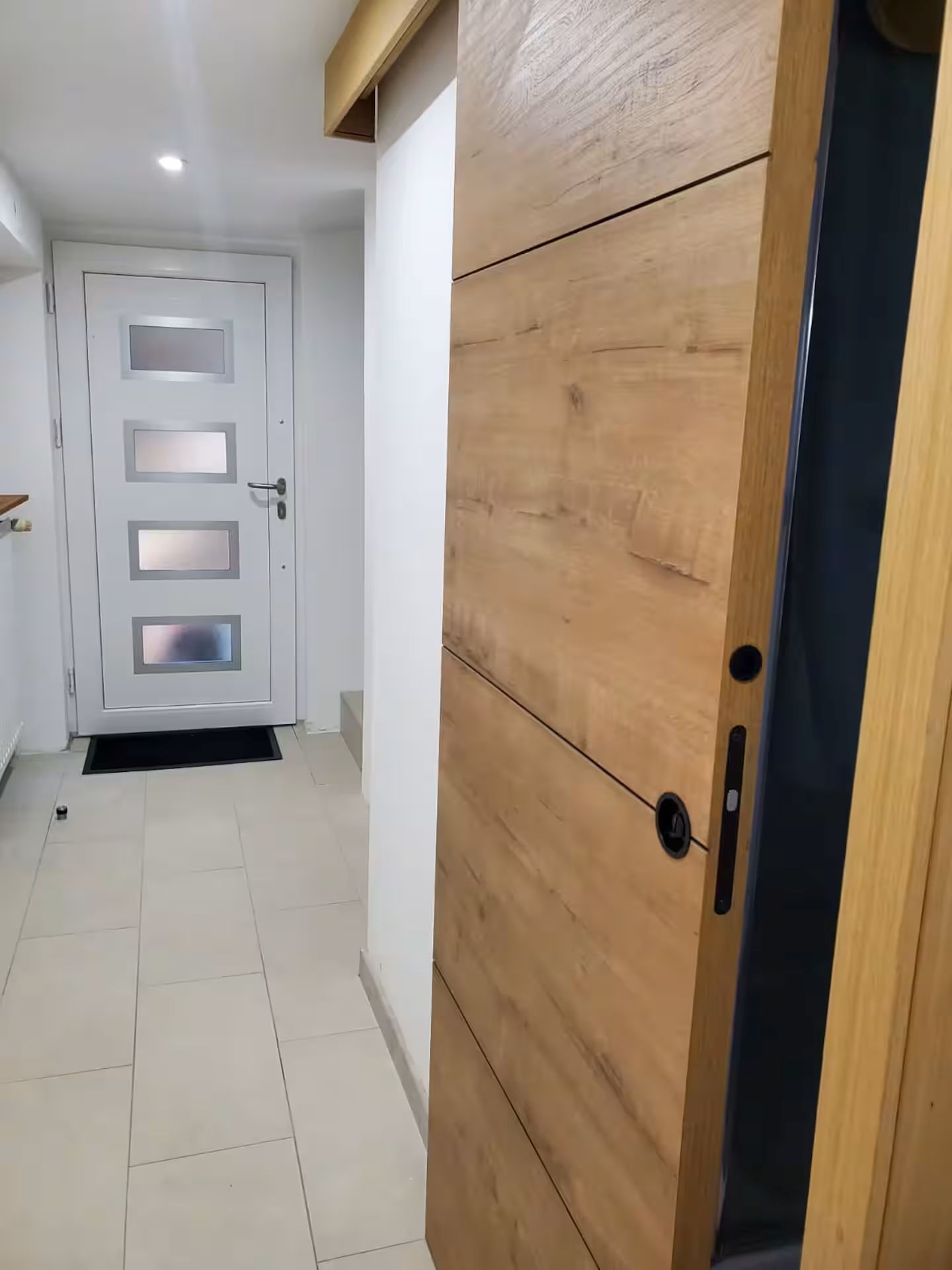 Un couloir avec une porte en bois et une porte blanche dotée de panneaux en verre dépoli.