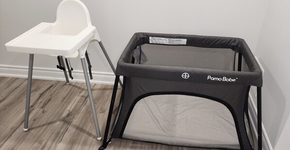 A baby playpen with a white high chair beside it.