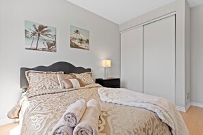 A neatly made bed with rolled towels, a bedside lamp, and two wall art pieces depicting palm trees.