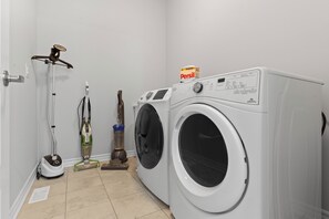 A laundry room with a front-loading washing machine, a vacuum cleaner, and a steam cleaner.