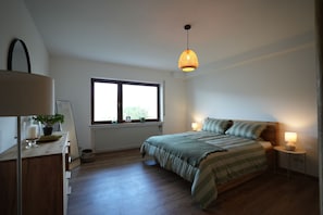 Quarto com cama, mesas de cabeceira, janela e luminária pendente.