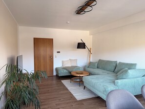 Uma sala de estar moderna com sofá, uma mesa redonda pequena, televisão e planta em vaso.