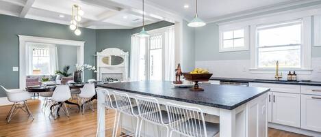 A modern kitchen with a central island, white cabinetry, and a dining area with white chairs.