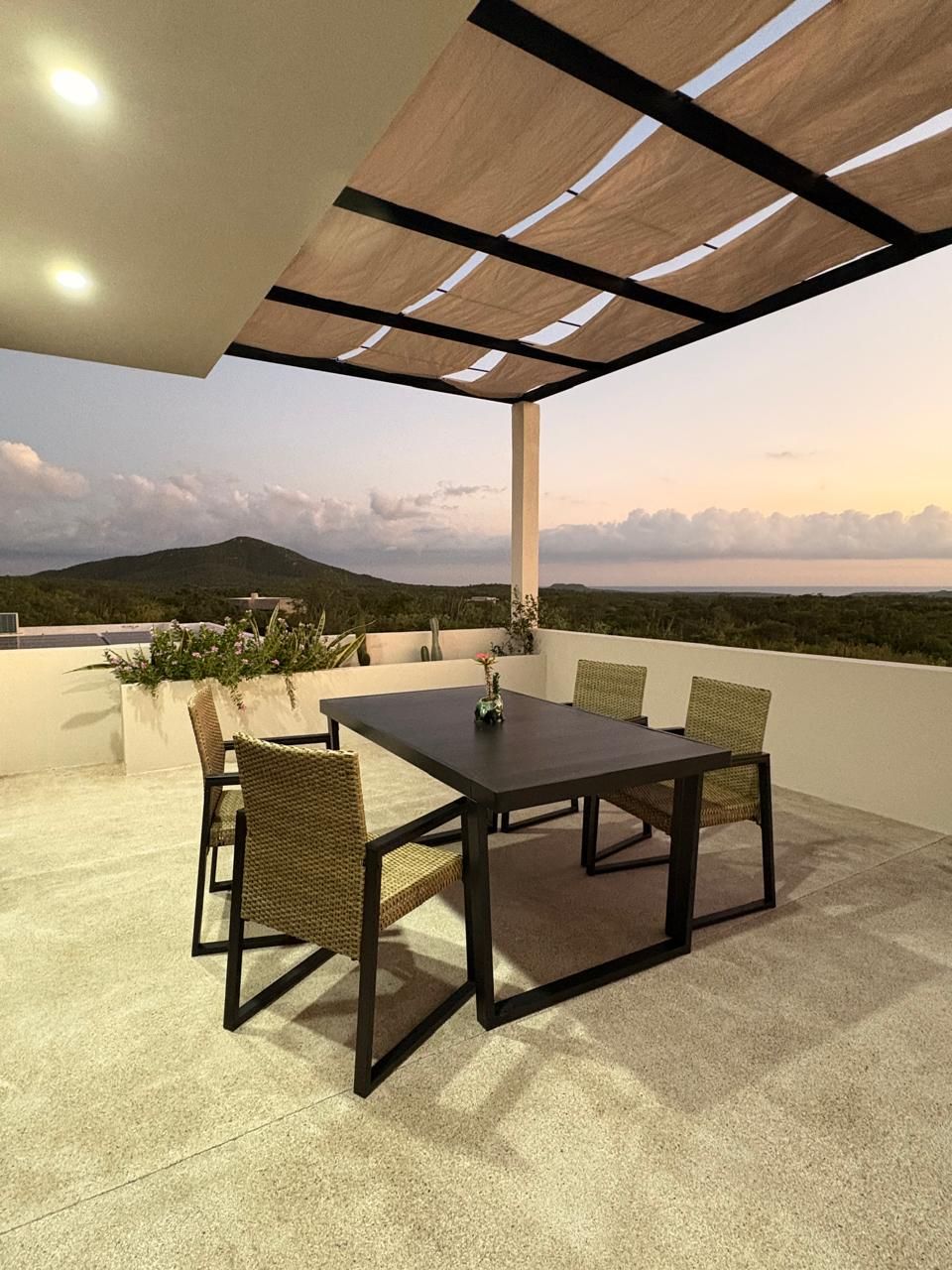 Eine Außenpatio mit Tisch und Stühlen, einer Pergola darüber und Blick auf eine entfernte Landschaft.