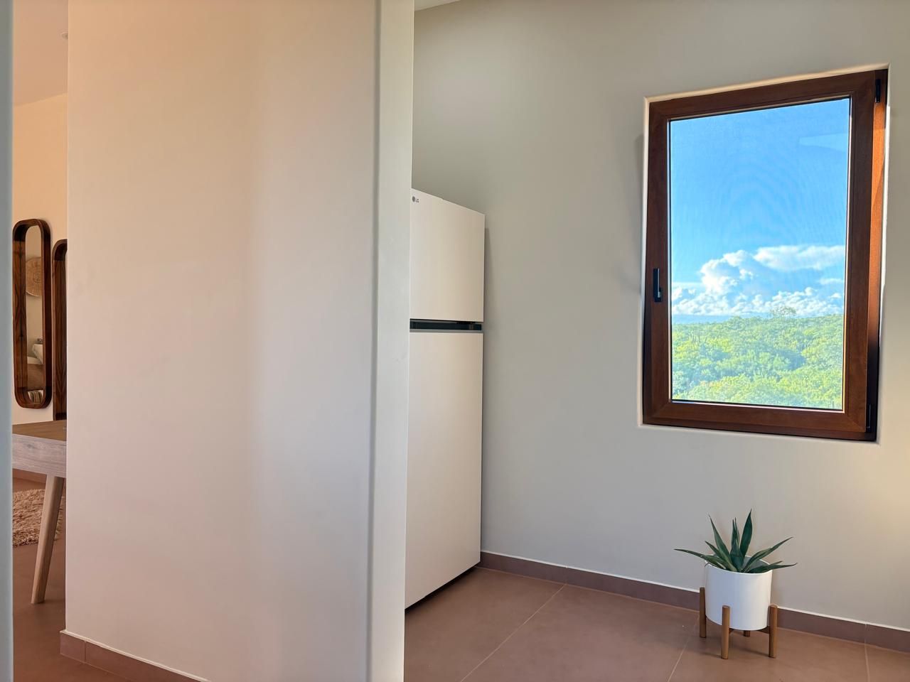 Ein Zimmer mit Blick auf einen Wald, ein weißes Schränkchen und ein Blumentopf.