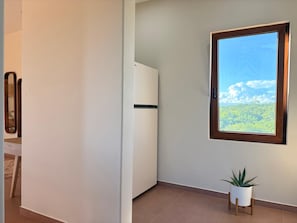 Quarto com vista para uma floresta através de uma janela, um armário branco e um vaso de planta.