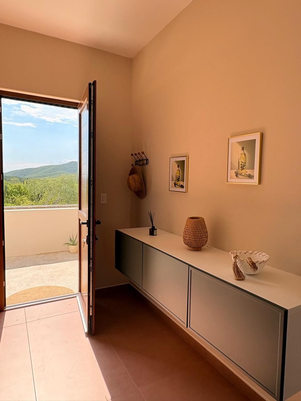 Una habitación con puerta corredera que da a un balcón, una encimera alargada con objetos decorativos y cuadros en la pared.