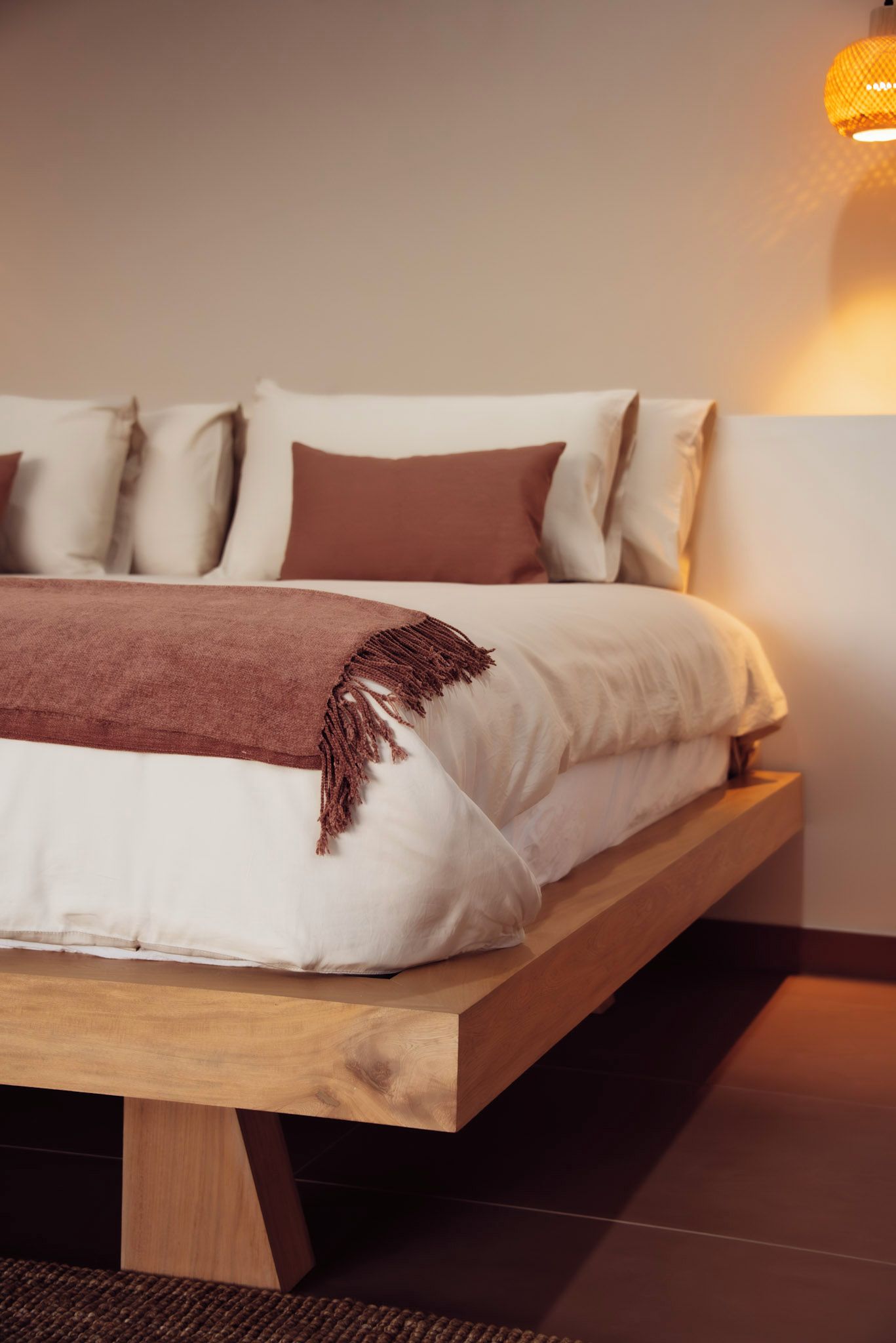Een bed met een houten frame, wit beddengoed en een bruine plaid.