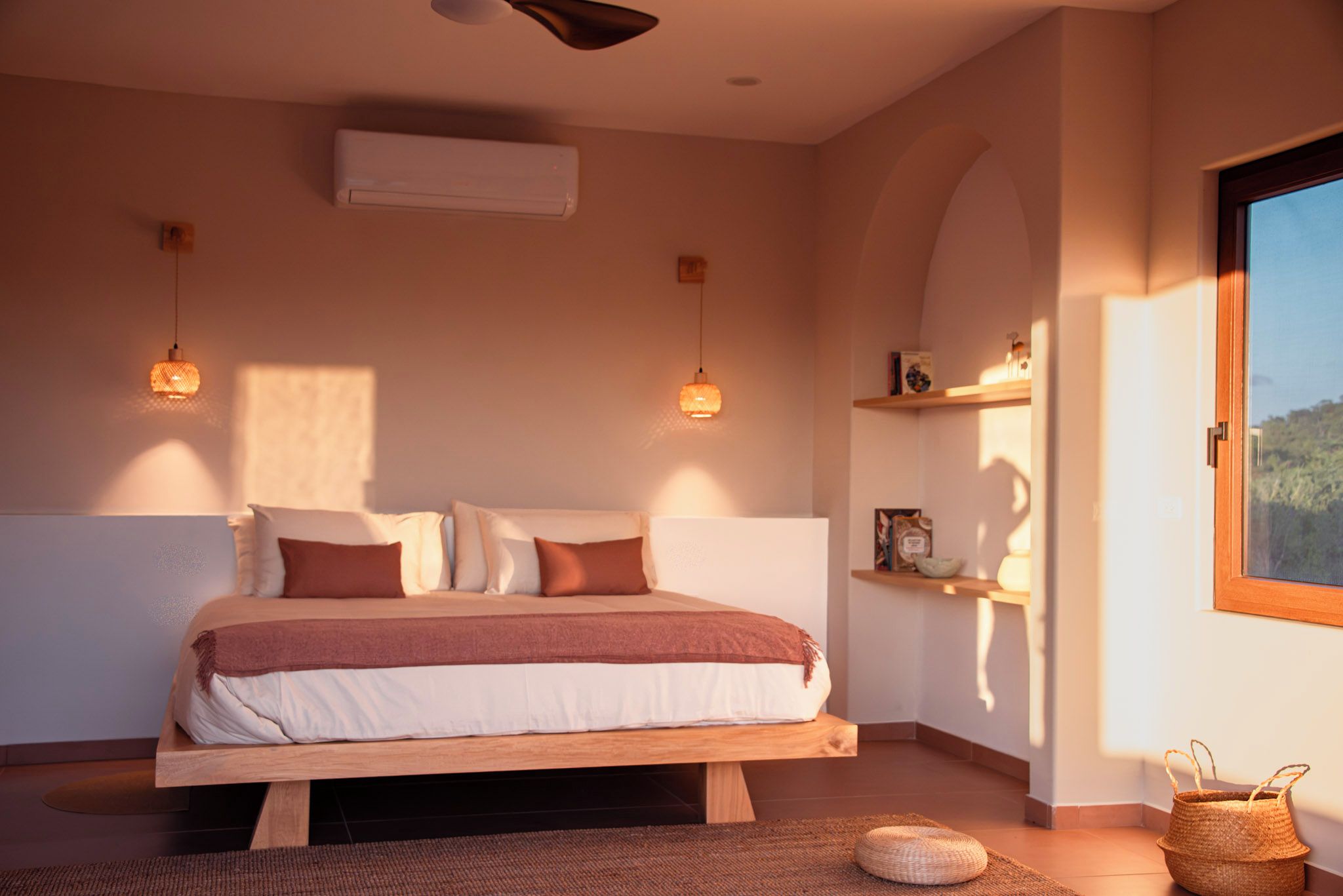 A bedroom with a bed, bedside lamps, a window, and a shelf with items.