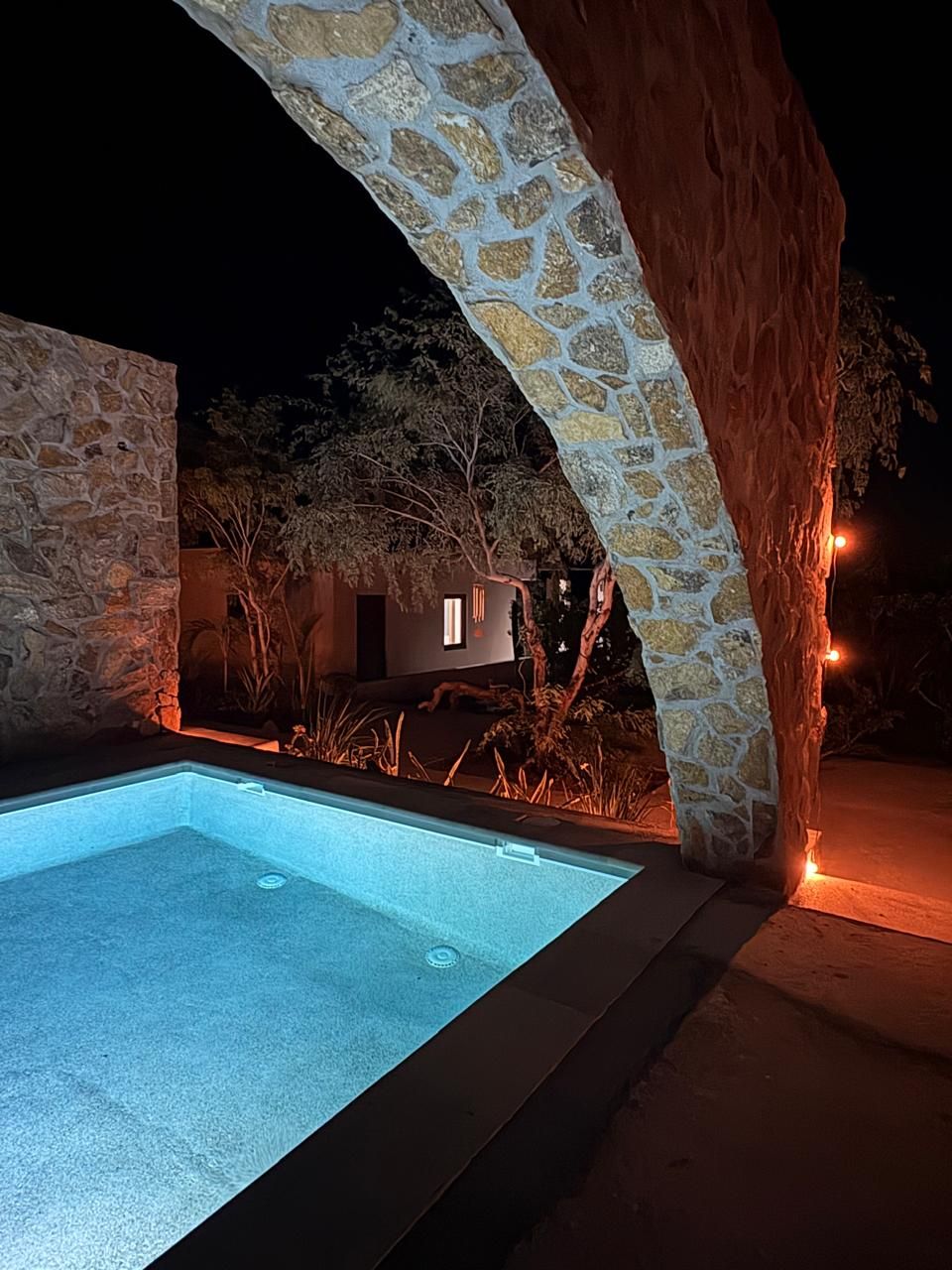 Un arco de piedra que da acceso a una zona de piscina por la noche.