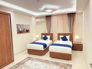 A hotel room with two beds, a wooden wardrobe, a painting, an air conditioning unit, and a window with curtains.